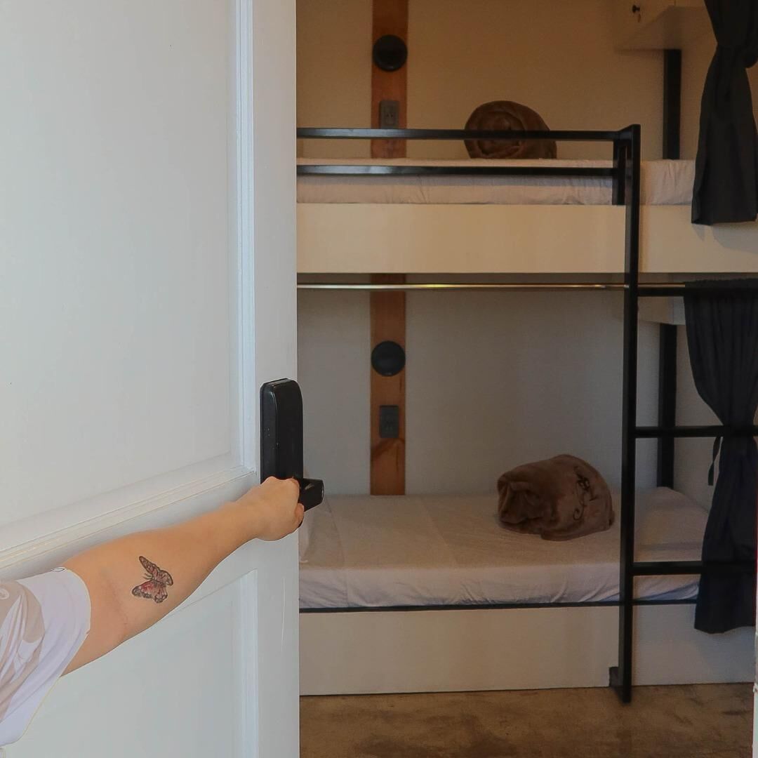 Habitación con literas y una mano sujetando el pomo de una puerta.