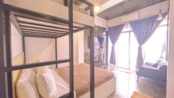 Quarto com beliche, escrivaninha e cadeira, sofá e uma janela grande com cortinas.