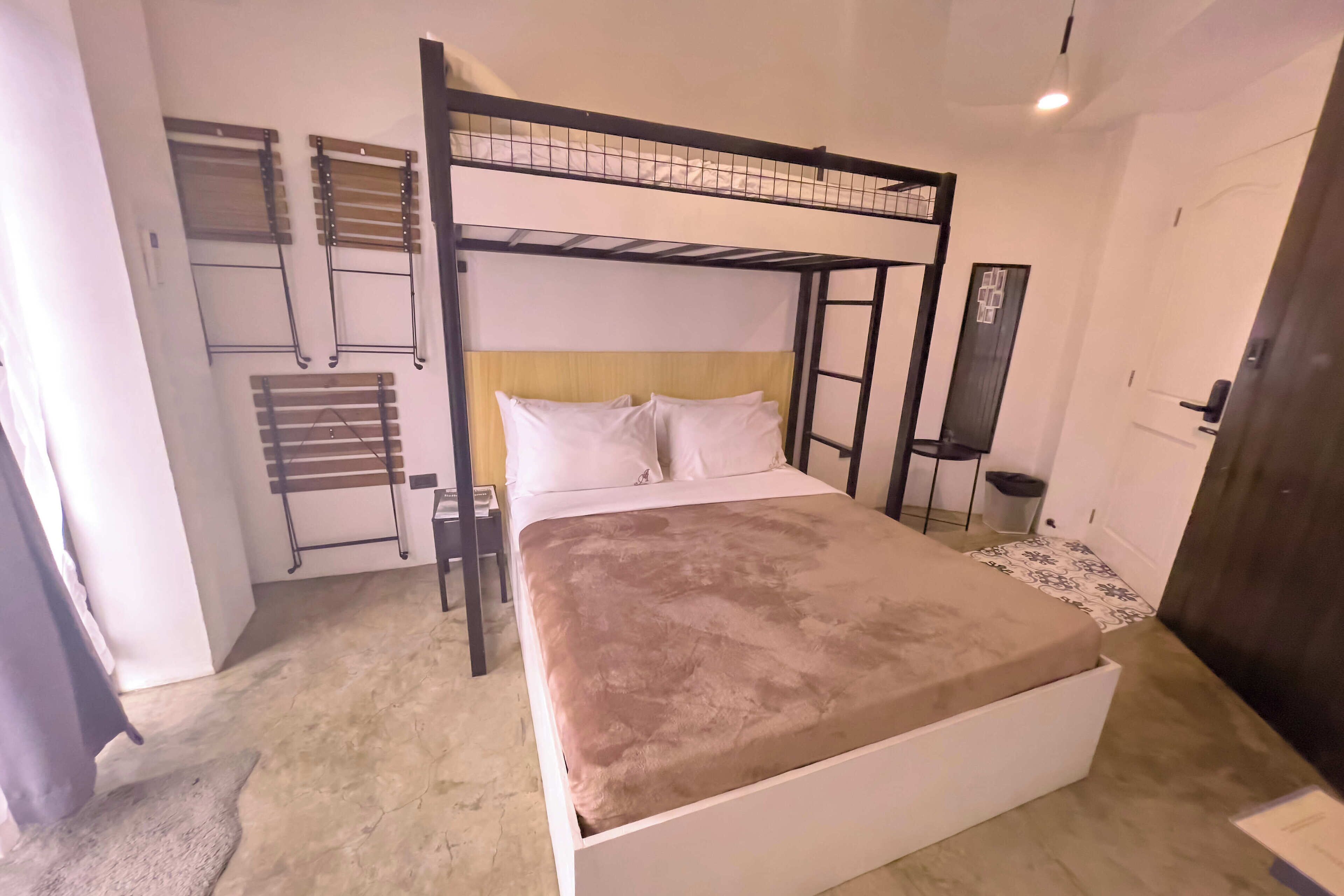 A bunk bed with a white headboard, a single bed with a brown blanket, a small table, and a wall-mounted drying rack.