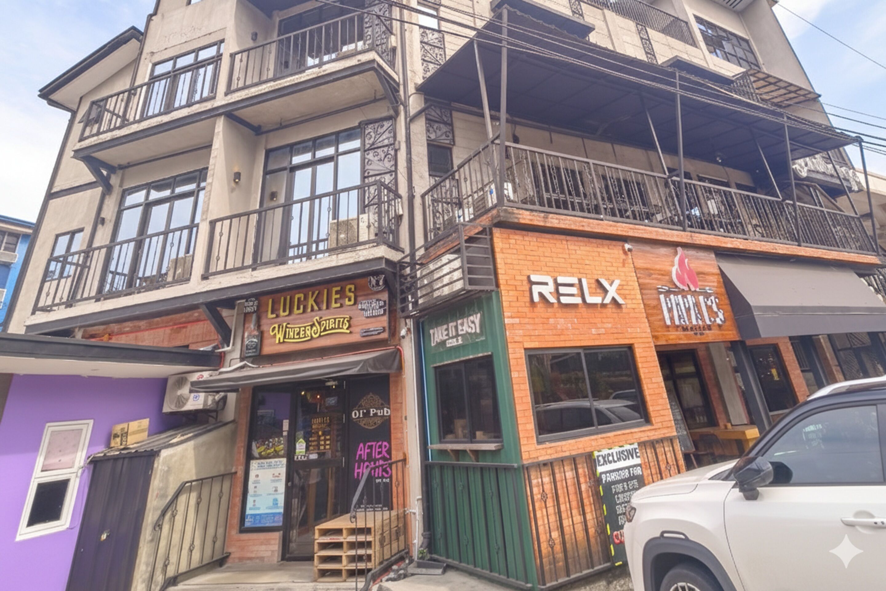Een meerhoog gebouw met verschillende bedrijven, waaronder een pub genaamd 'Luckies' en een winkel met de naam 'Relax'.