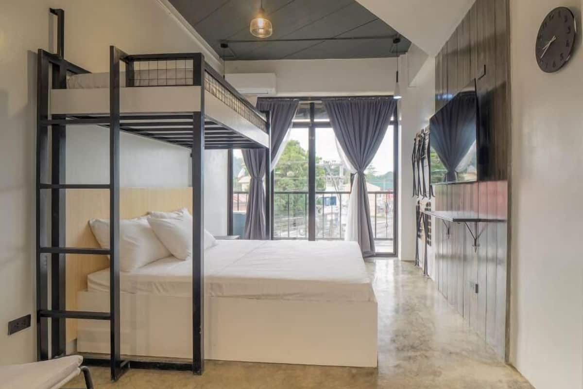 Una camera con un letto a castello, un letto matrimoniale, una TV e un'ampia finestra con tende.