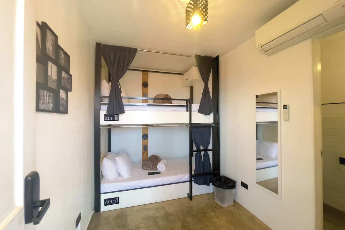 Camera con letto a castello, illuminazione a soffitto, condizionatore d'aria a parete e una piccola finestra con cornice bianca.
