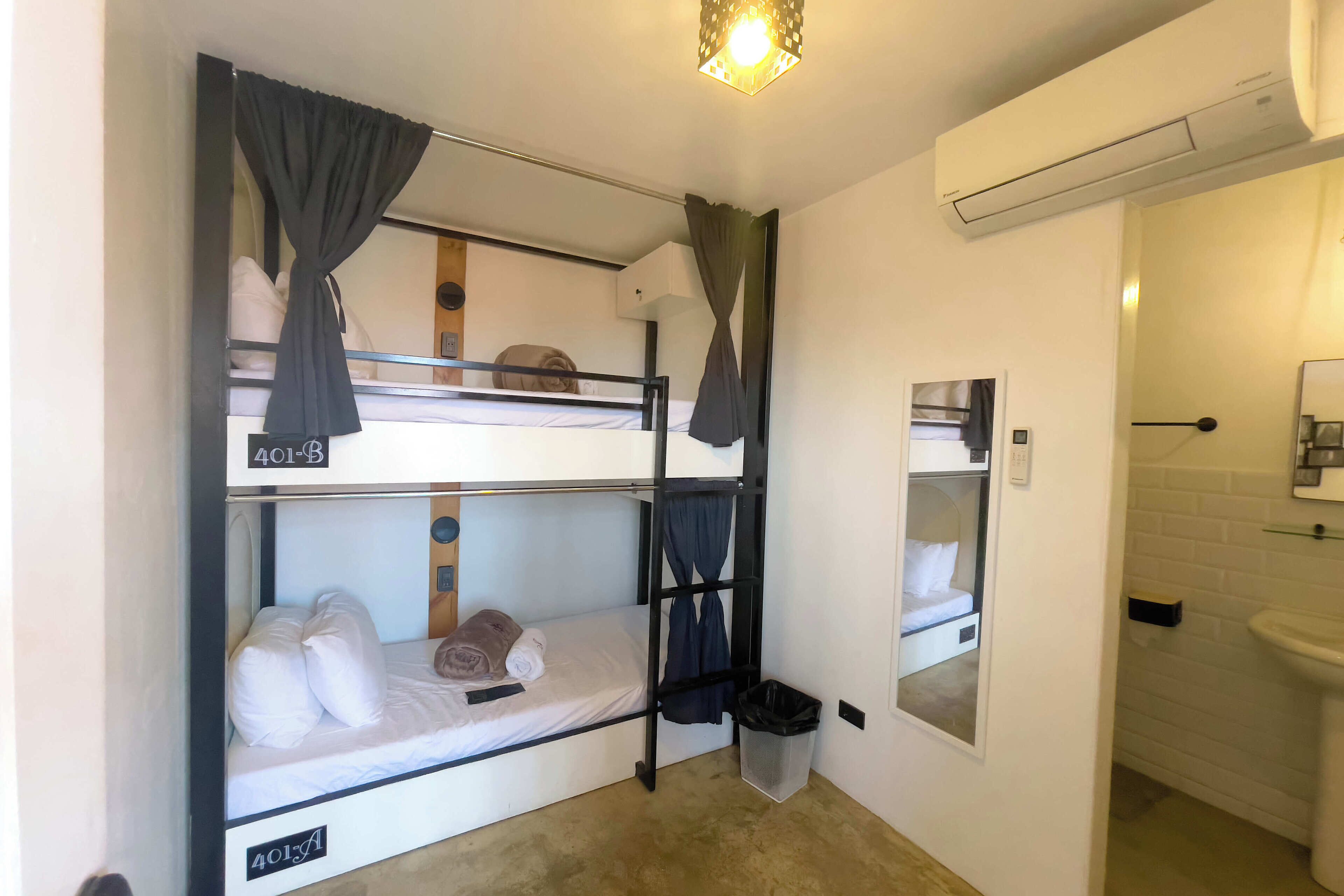 A bunk bed room with a small trash bin and a bathroom with a sink and mirror.