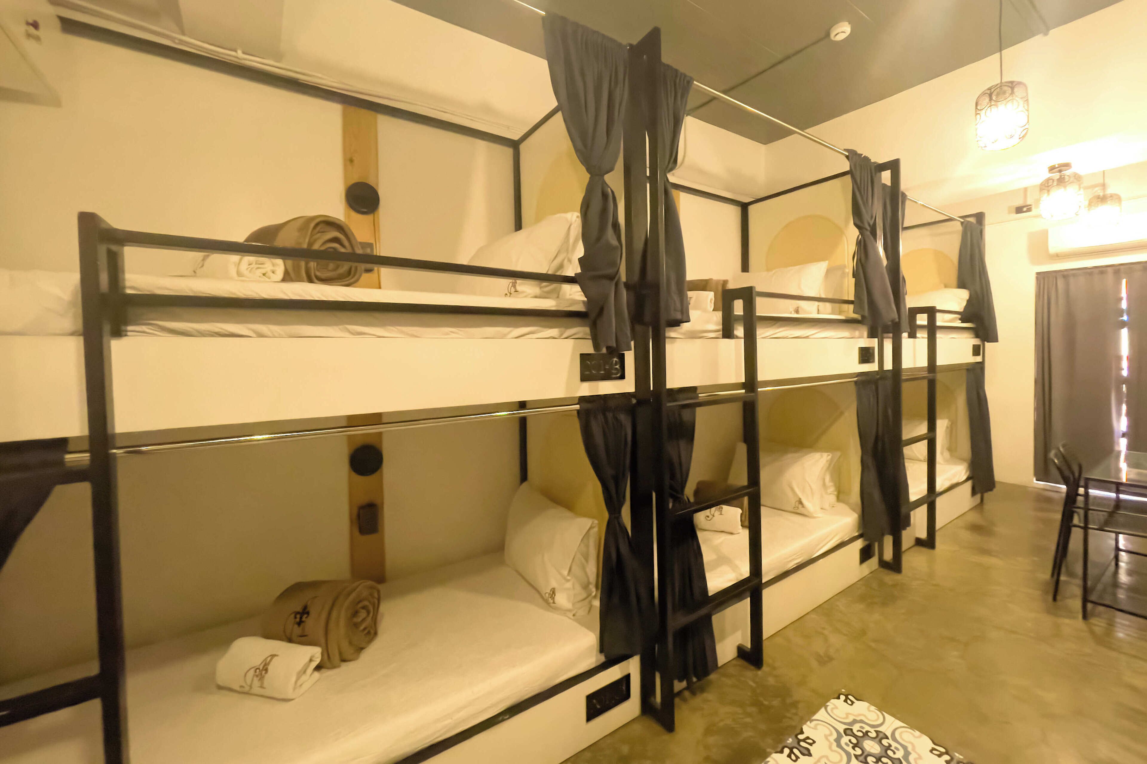A bunk bed room with a desk and chair, curtains, and a small table.