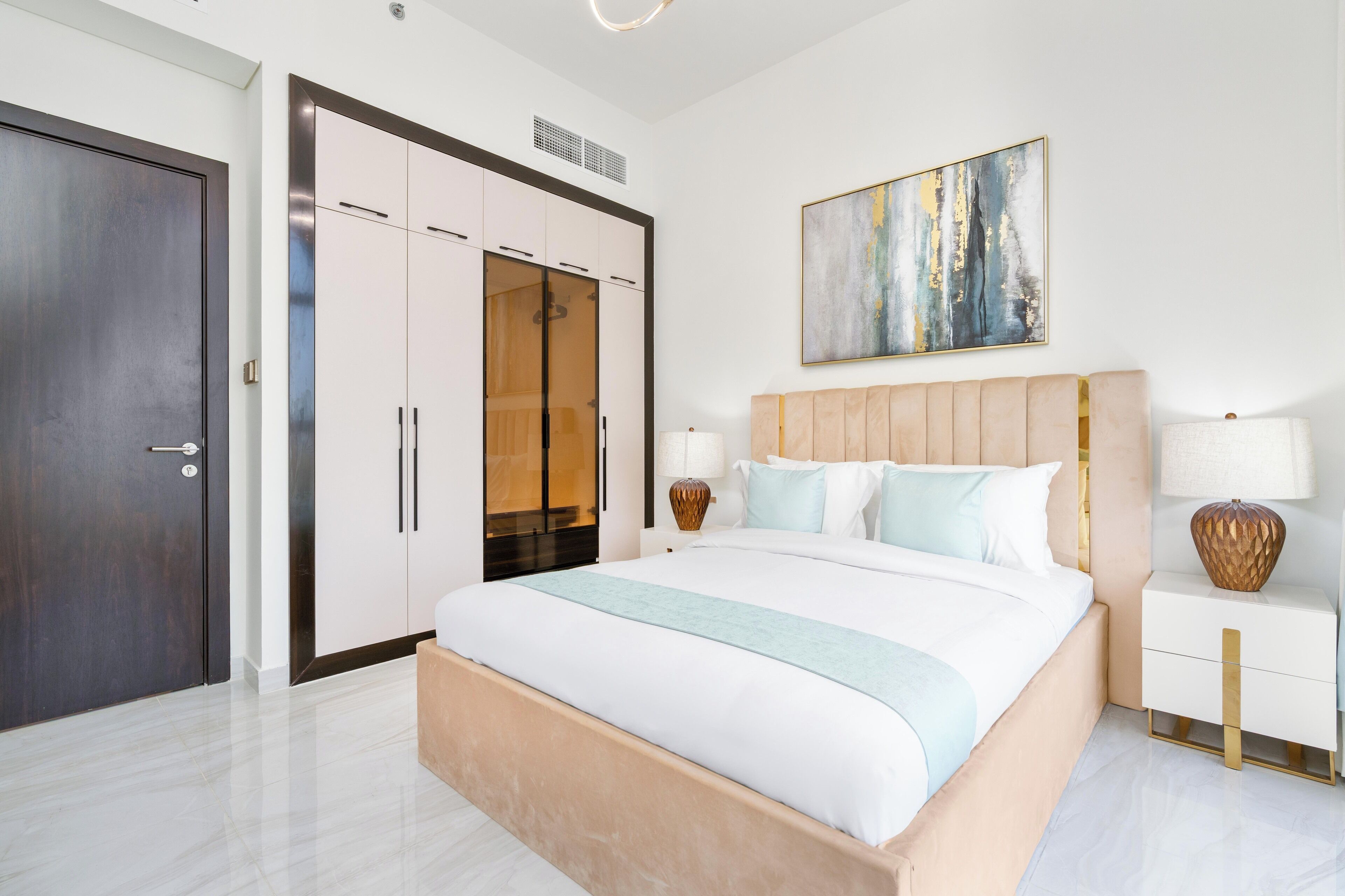 A modern bedroom with a large bed, a wardrobe, a bedside table, and a wall-mounted abstract painting.