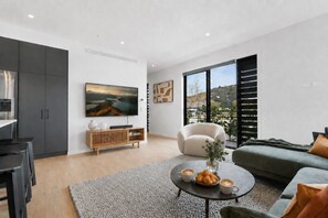 A modern living room with a large TV, a sofa, a coffee table with pastries, and a view of the outdoors.