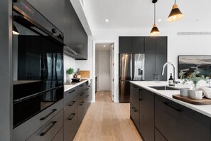 A modern kitchen with dark cabinetry, stainless steel appliances, and pendant lighting.