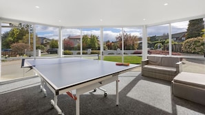A ping pong table in a room with large windows, a wicker sofa, and a view of a residential area.