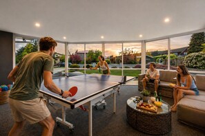 A ping pong table in a room with large windows, a wicker coffee table, and a sofa.