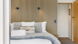 A bedroom with a bed, pillows, a wooden slat wall, and a door.