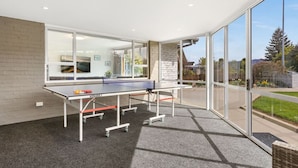 A ping pong table in a room with large windows, carpeted floor, and a brick wall.