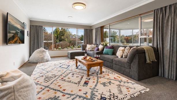A modern living room with a grey sofa, a coffee table, and a large window offering a view of the outdoors.