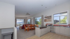 A modern kitchen with a dining area, large windows, and a view of the outdoors. - Amazing views of Lake and Mountains on Bovett (Wānaka)