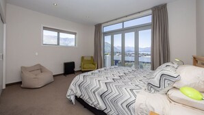 A bedroom with a large bed, a bean bag chair, a view of mountains through a window, and a chair by the window. - Amazing views of Lake and Mountains on Bovett (Wānaka)