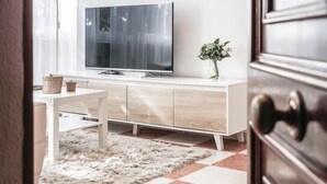 Una sala de estar moderna con un televisor de pantalla plana grande, un sofá blanco y una mesita pequeña.