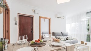 Un comedor con una mesa de madera dispuesta para cuatro personas, un frutero y un sofá al fondo.
