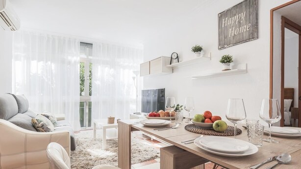 Una sala de estar moderna con un sofá, una mesa de comedor para cuatro personas y una cocina visible a través de una puerta de vidrio.