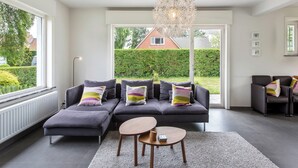 A modern living room with a sectional sofa, a round coffee table, and a unique chandelier. - Renovated villa with large garden (Koksijde)
