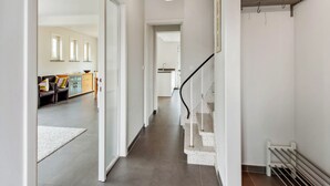 A hallway with a white staircase, a radiator, and a hanging light fixture. - Renovated villa with large garden (Koksijde)