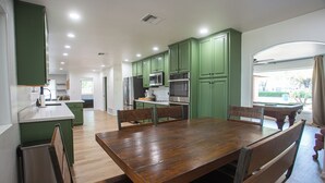 Una cocina amplia con armarios verdes, una mesa de comedor de madera y vistas al exterior.