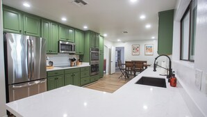 Una cocina moderna con armarios verdes, electrodomésticos de acero inoxidable y una encimera de mármol blanco.