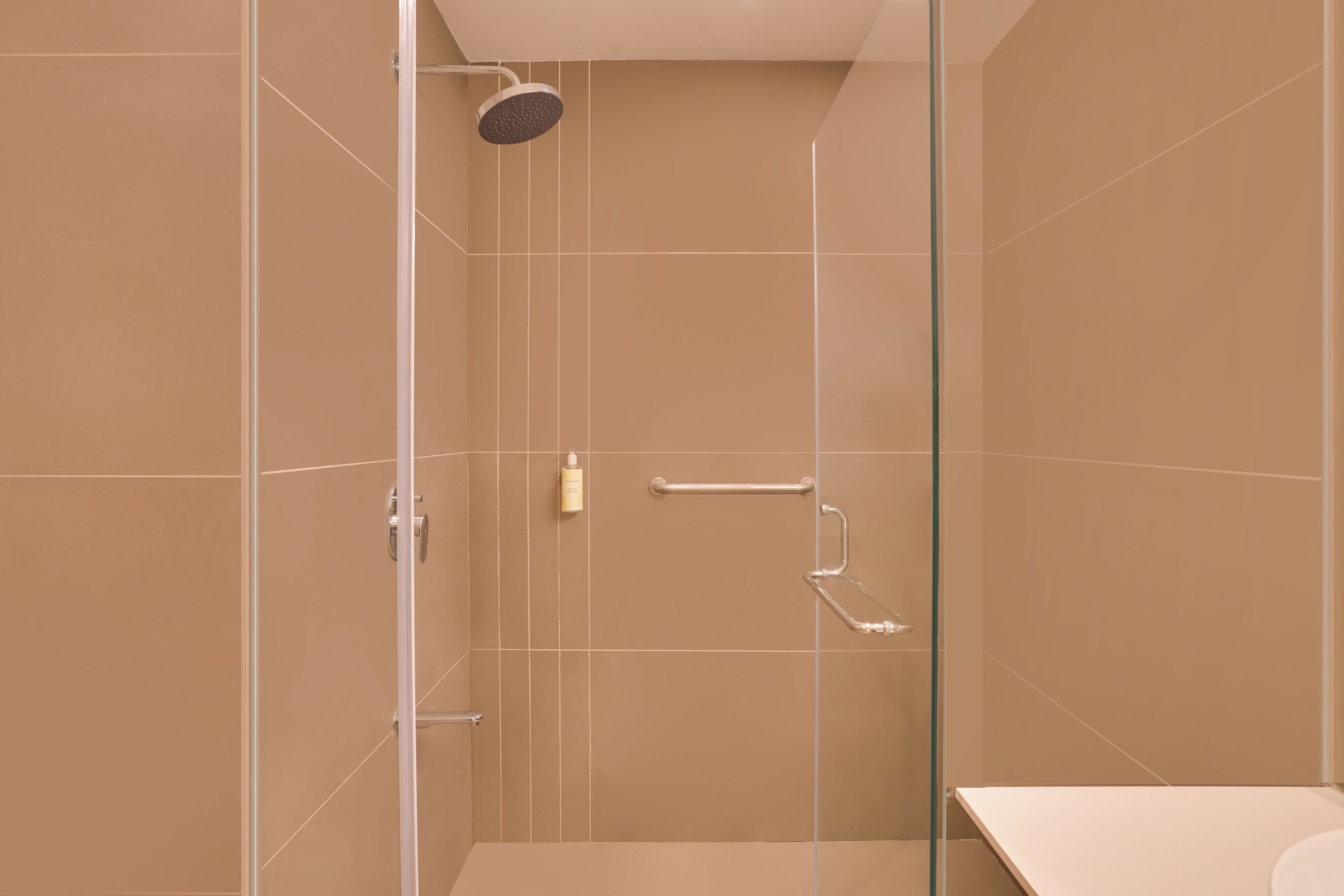 A modern bathroom with beige tiles, a glass shower enclosure, and a white countertop.