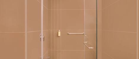 A modern bathroom with beige tiles, a glass shower enclosure, and a white countertop.