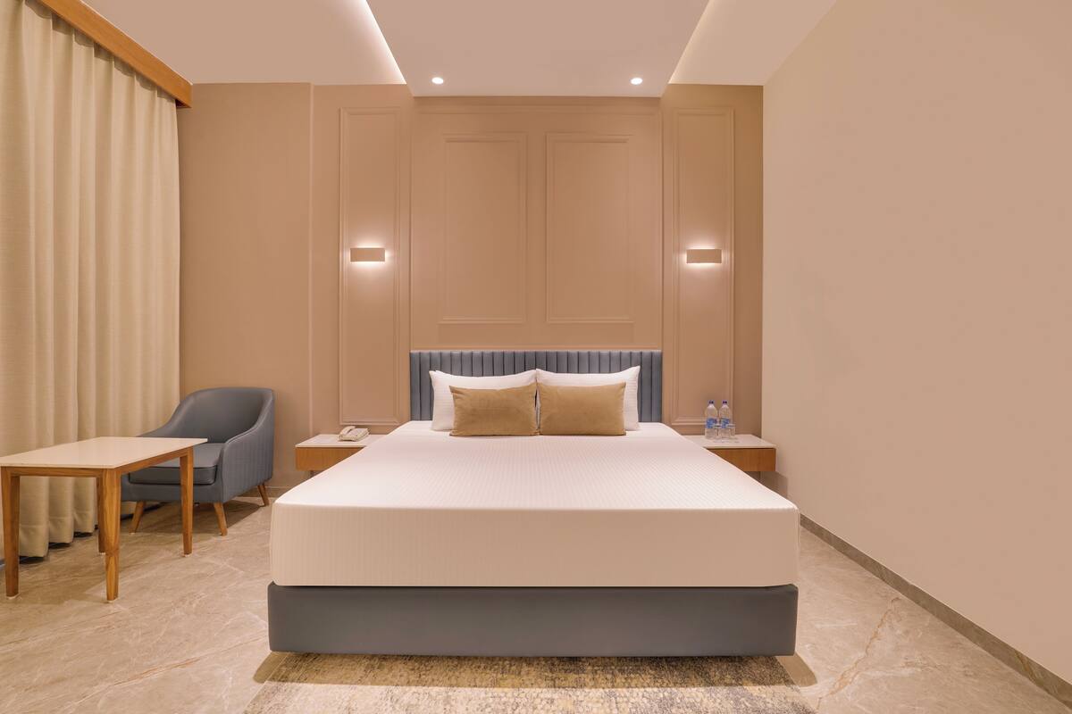 Une chambre d’hôtel avec un grand lit, une chaise, une petite table et une table de chevet avec une lampe.