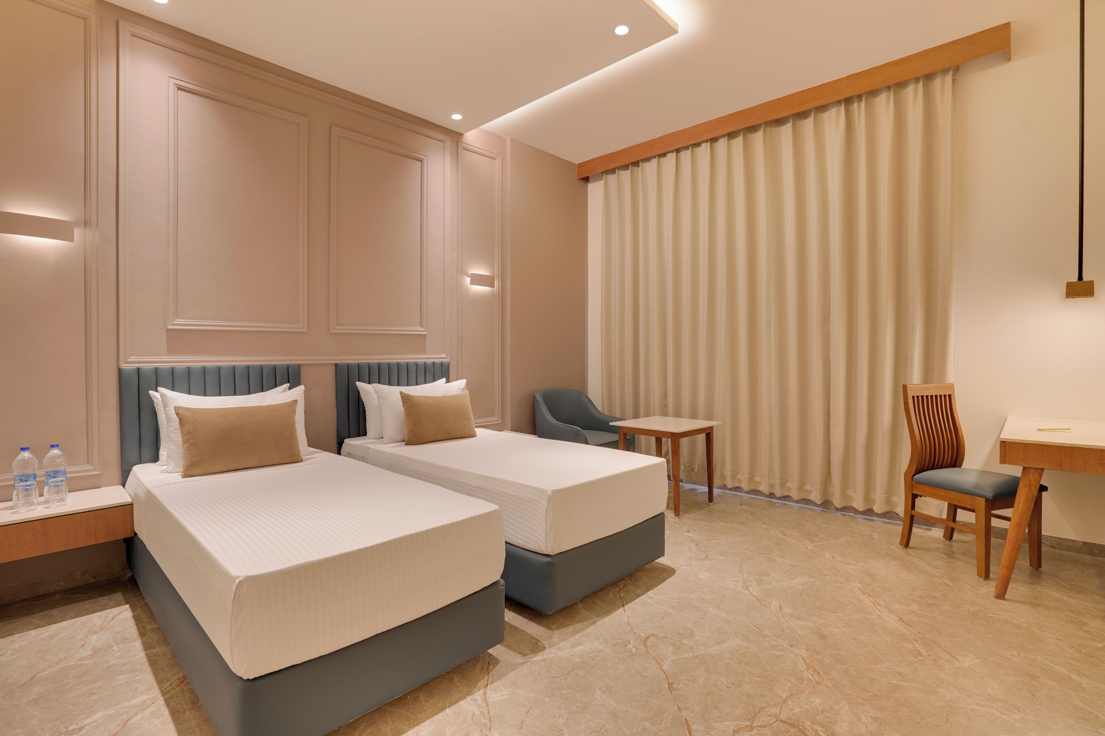 A hotel room with two beds, a desk, a chair, a nightstand, and a curtain.