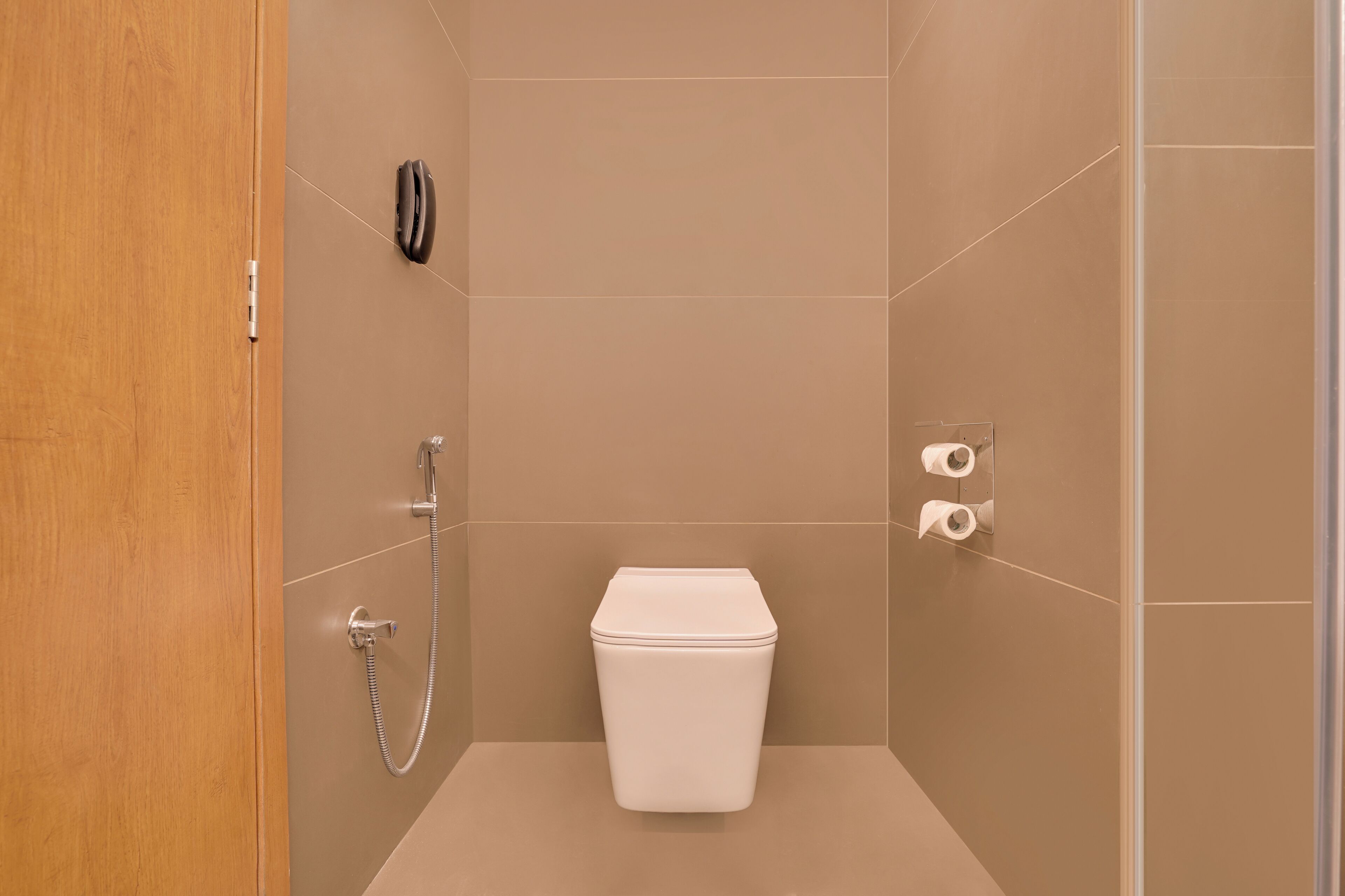 Une petite salle de bain moderne, équipée de toilettes, d’une douche et d’une porte en bois.