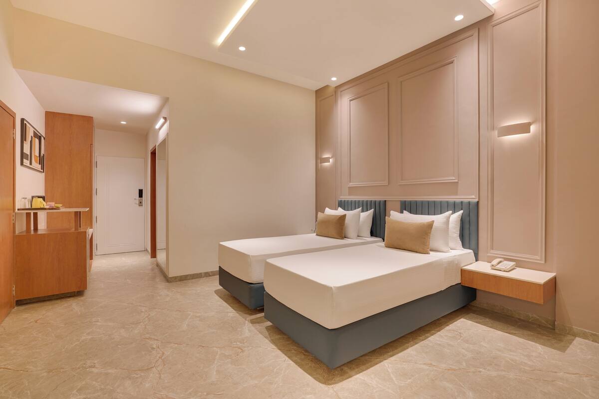 Une chambre d’hôtel moderne avec deux lits simples, un bureau en bois et une armoire intégrée.