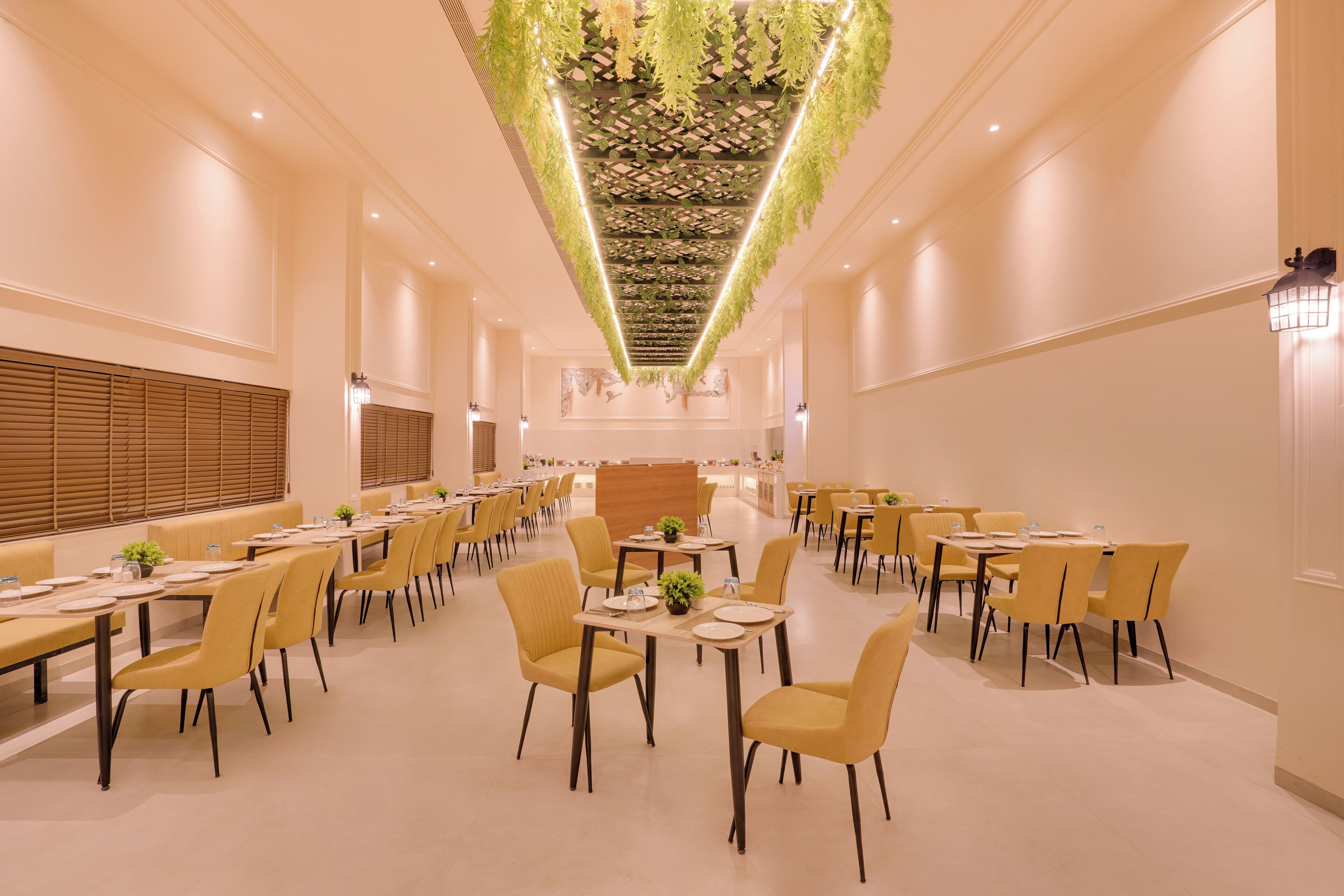 Un amplio comedor con varias mesas y sillas, un mostrador de recepción central e instalación de plantas colgantes en el techo.
