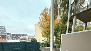 Uma varanda com duas poltronas de vime, vista para a cidade e uma cerca verde ao fundo.