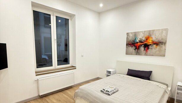 Quarto com cama, janela, pintura e radiador branco.
