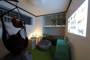 A child's playroom with a hanging swing, bean bag, and a projector screen displaying animal images.