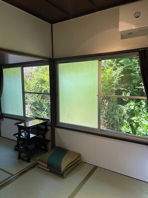 Una tradizionale stanza giapponese con pavimento in tatami, un tavolino basso, cuscini e ampie finestre con vista sul verde.