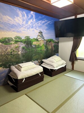 Een kamer met tatami vloeren, twee bedden met witte beddengoed, een aan de muur bevestigde televisie en een muurschildering van een kasteel.