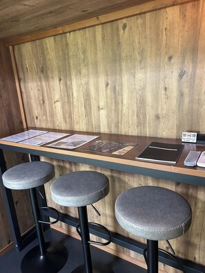 Un'area bar con parete in legno, un bancone con menù e tre sgabelli grigi.