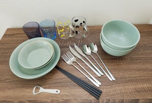 A wooden table with a set of plates, bowls, glasses, and cutlery.
