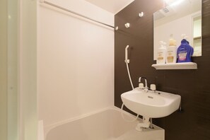 Un baño con lavamanos blanco, un espejo y ducha. Hay artículos de aseo en un estante.