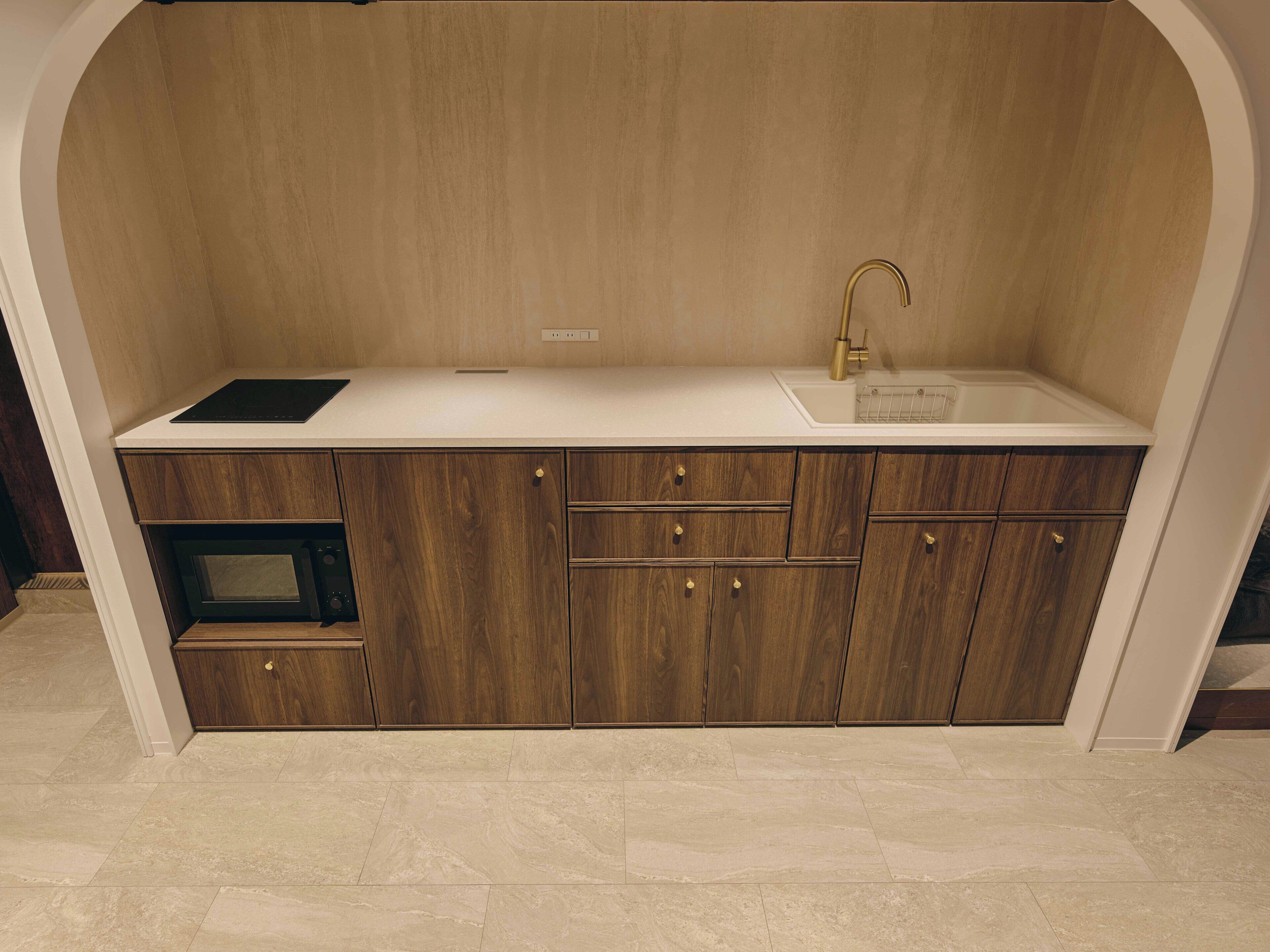 A compact kitchen with a built-in microwave, a sink with a gold faucet, and wooden cabinets.