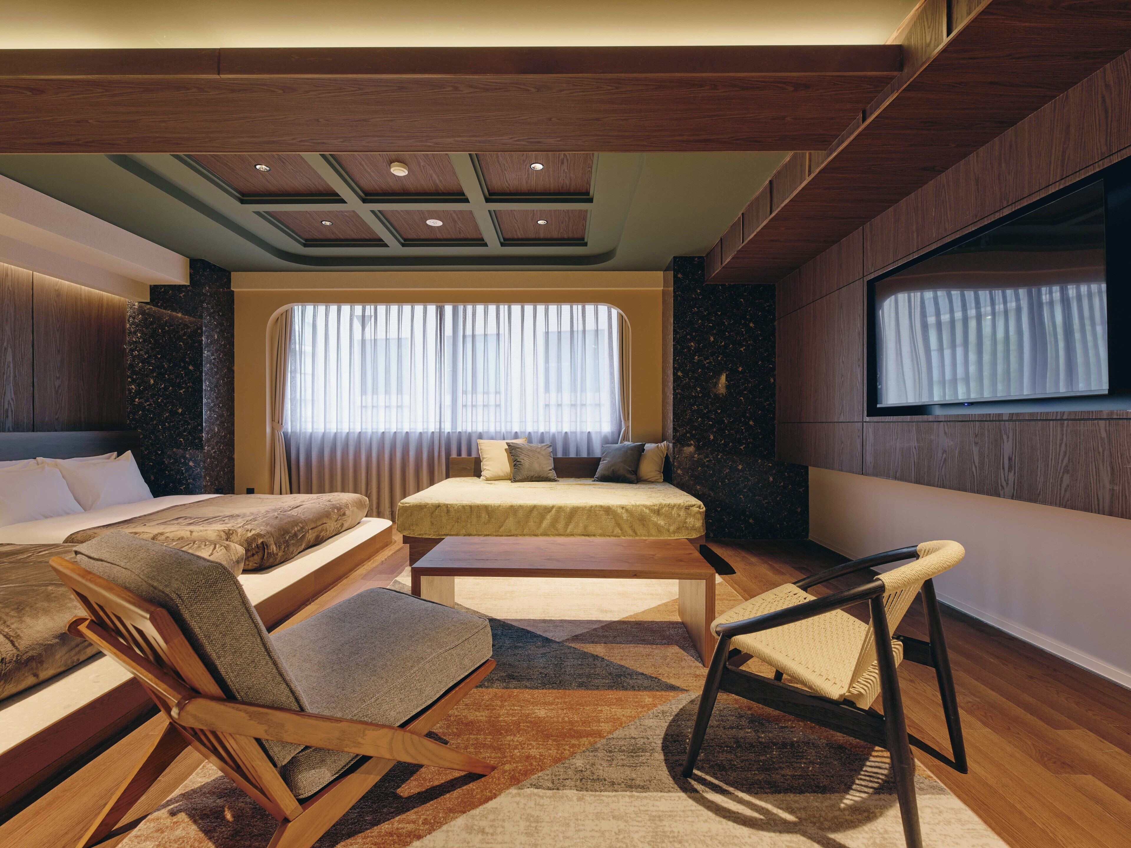 A modern bedroom with a large bed, a smaller bed, a sofa, and a TV.