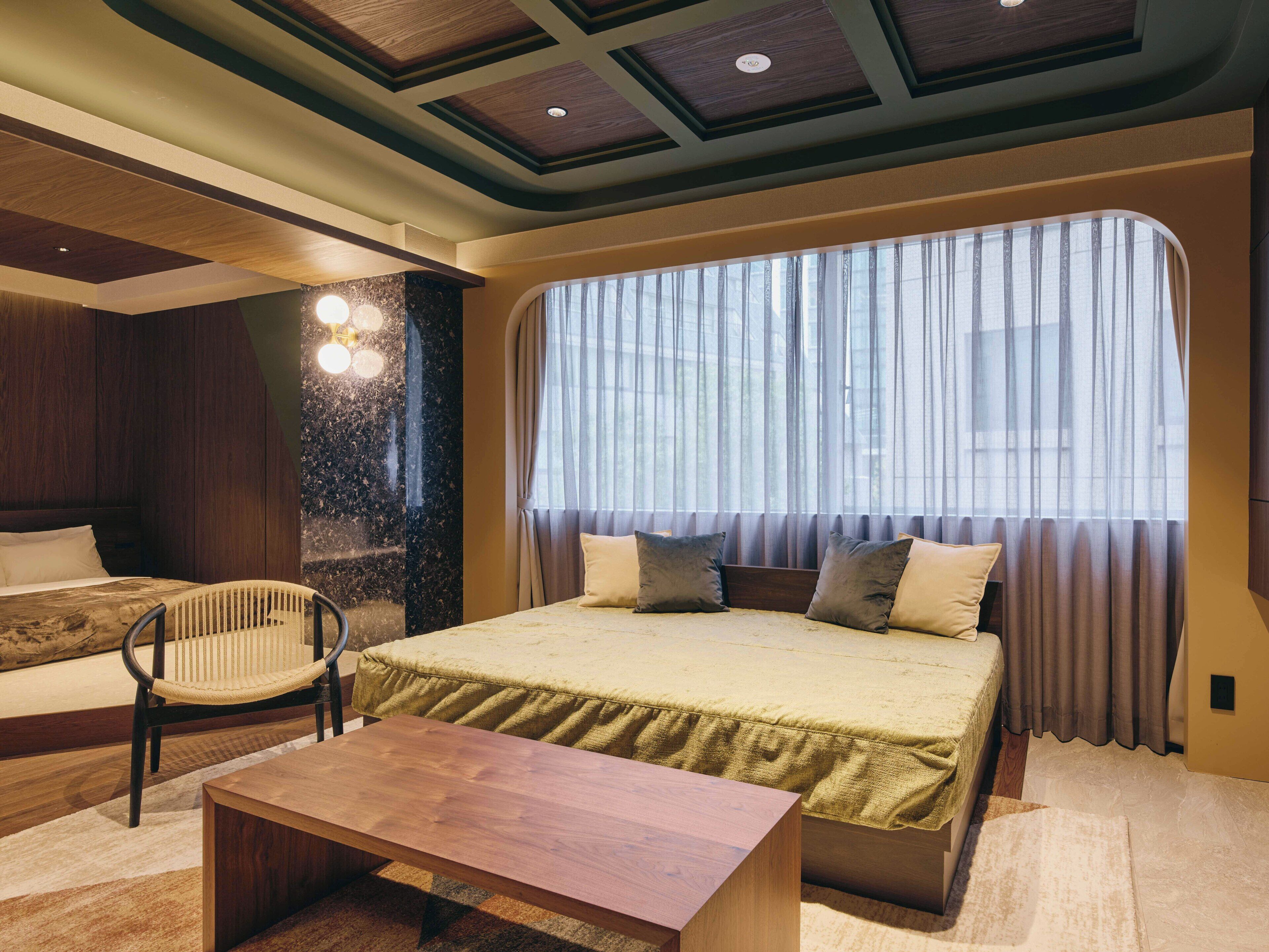 A modern bedroom with a large bed, a wooden nightstand, a chair, and a large window with curtains.