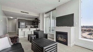 Una sala de estar moderna con chimenea, un televisor de pantalla plana y vista a un estacionamiento a través de amplias ventanas.