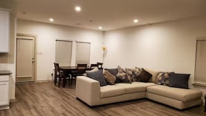 Ein modernes Wohnzimmer mit einem beigefarbenen Ecksofa, einem Esstisch mit Stühlen und einer Stehlampe.