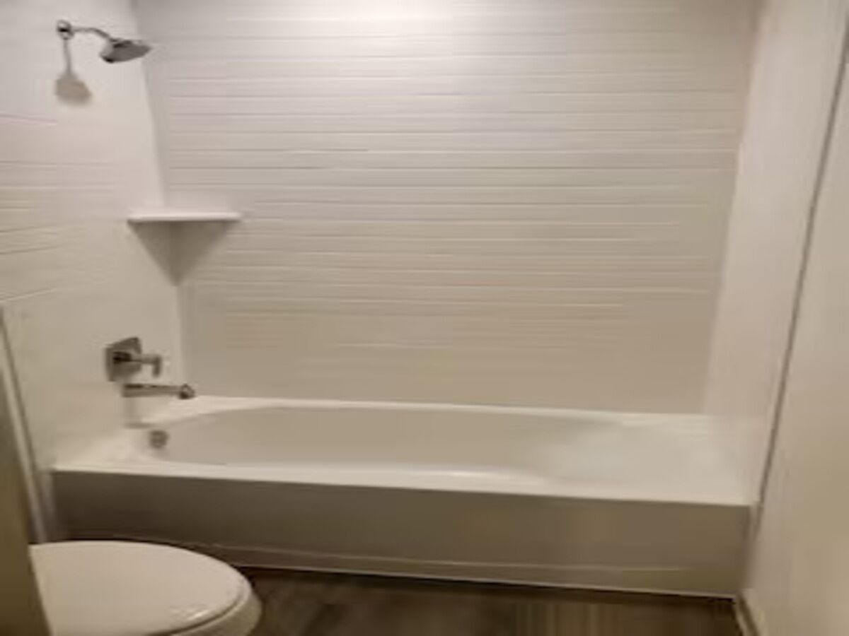 Et badeværelse med badekar, toilet og brusehoved.