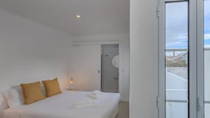 A bedroom with a bed, two pillows, a bedside lamp, and a view of a bathroom and outside. - GuestReady - Casa Irmãs (Ponta Delgada)