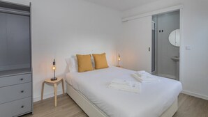 A hotel room with a bed, a wardrobe, a bedside table with a lamp, and a bathroom visible through an open door. - GuestReady - Casa Irmãs (Ponta Delgada)