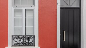 A building with a red facade, a white window with a black metal balcony, and a black door with a gold handle. - GuestReady - Casa Irmãs (Ponta Delgada)