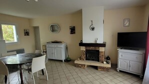 A kitchen with a fireplace, a dining table with chairs, a TV, and a window. - Quiet, detached house close to shops and hiking trails. (Forcalquier)